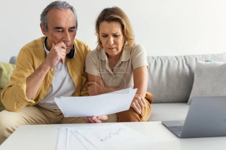 Photo for Upset married senior spouses looking at loan documents, checking financial papers and planning budget at home. Stressed elderly husband and wife suffering crisis while calculating family spends - Royalty Free Image