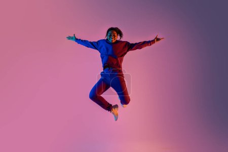Foto de Longitud de cuerpo completo disparo de dama negra saltando sobre fondo de luz de neón vivo rosa. Concepto de danza, juventud, afición, dinámica, movimiento, acción, anuncio - Imagen libre de derechos