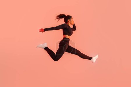 Photo for Athlete black woman in sportswear jumping and having workout on red neon studio background, side view, copy space, full length. Sport and fitness concept - Royalty Free Image