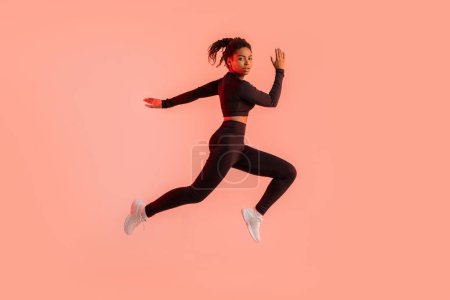 Téléchargez les photos : Jeune femme noire sportive s'entraînant sur fond de studio néon rouge, courant et regardant la caméra, pleine longueur. Sport moderne, action, concept de mouvement - en image libre de droit