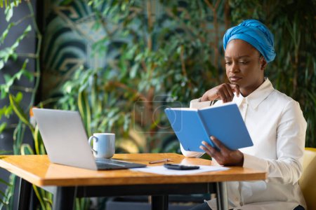 Photo for Stressed young african american lady accountant preparing for audit, reviewing her financial notes, calculating expenses. Analyst working remotely at cafe, using laptop, calculator, copy space - Royalty Free Image