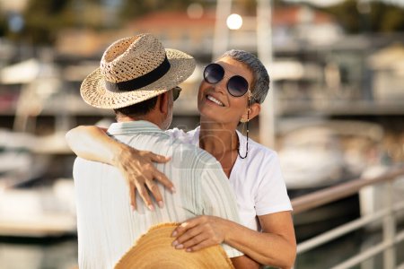 Photo for Summer Delights. Loving Mature Couple Hugging At Marina Port With Luxury Yachts and Sailboats Outside, Showcasing Golden Love, Enjoying Seaside Vacation On Sunny Day At Pier, Wearing Sunglasses - Royalty Free Image