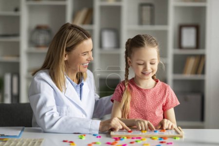 Photo for Dyslexia Treatment. Pediatric Neurologist Lady Having Therapy Session With Cute Little Girl, Smiling Female Child Making Word With Colorful Letters On Table, Improving Reading Skills, Closeup - Royalty Free Image