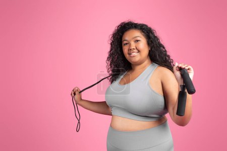 Photo for Satisfied black woman plus size in sportswear with skipping rope ready to training on pink background, smiling at camera, free space. Cardio active workout, weight loss and fitness - Royalty Free Image