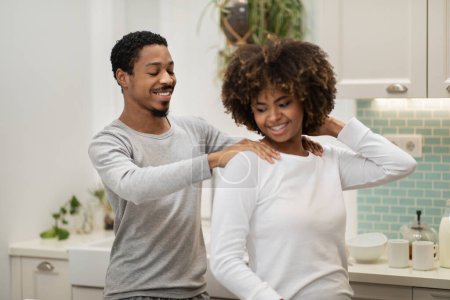 Photo for Happy loving handsome young black boyfriend giving girlfriend neck and shoulders massage. Cheerful afican american couple spend time together at home, modern kitchen interior. Relationships concept - Royalty Free Image