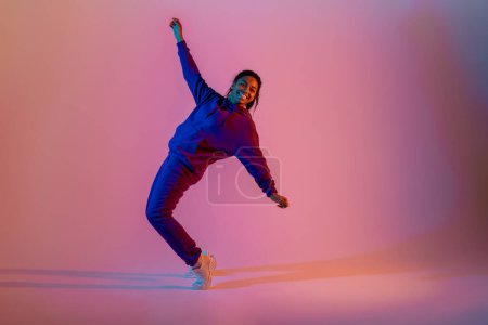 Photo for Sport dancing. Athletic and graceful black lady in sportwear dancing on pink background in neon light, full length, free space. Modern sport, action, motion, youth concept - Royalty Free Image