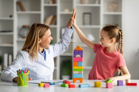 Photo for Cute Little Girl Giving High Five To Child Development Specialist During Meeting In Office, Smiling Therapist Lady Greeting Happy Female Kid With Progress, Celebrating Successful Therapy - Royalty Free Image