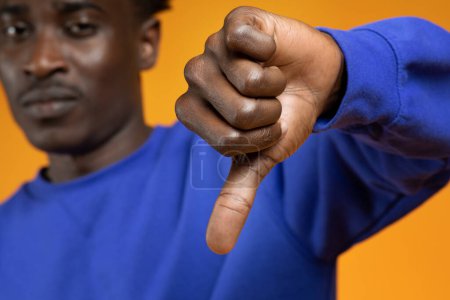 Photo for Sad disappointed african american young man showing thumb down, looking at camera isolated on yellow studio background, selective focus on guy hand. Negative opinion, dislike - Royalty Free Image