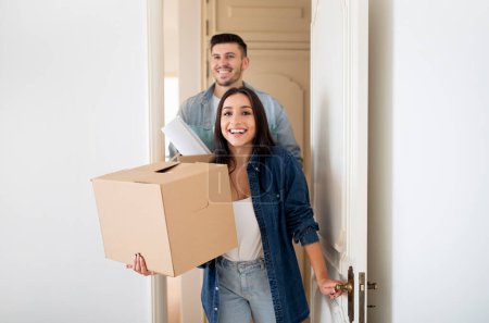 Photo for Young Happy Tenants Couple Entering Their New Home After Moving, Smiling European Spouses Opening Door And Carrying Boxes With Belingings, Excited Man And Woman Celebrating Relocation, Copy Space - Royalty Free Image