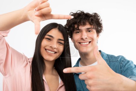 Téléchargez les photos : Happy Moment. Jeune couple encadrant leurs visages avec des doigts Cadre posant pour Selfie sur fond blanc, souriant à la caméra. Studio Portrait d'amis joyeux. Focus sélectif - en image libre de droit