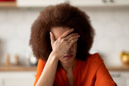 Photo for Closeup Portrait Of Upset Black Woman Covering Face With Hand, Depressed African American Female Making Facepalm Gesture While Sitting In Kitchen Interior, Suffering Depression Or Mental Breakdown - Royalty Free Image