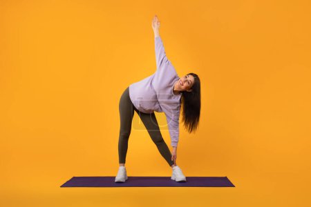 Photo for Prenatal fitness concept. Young pregnant lady staying active, stretching legs and hands during workout on yellow studio background, full length, free space - Royalty Free Image