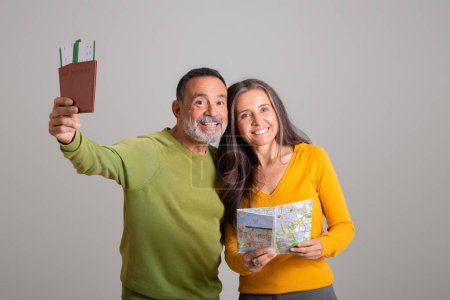 Photo for Satisfied european old husband and wife with map show passport and tickets on gray studio background. Couple enjoy travel, trip preparation, vacation planning together and lifestyle - Royalty Free Image