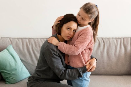 Photo for Worried serious caucasian little girl hugs and calms sad middle aged woman in living room interior. Support, love, relationship family, communication at home, help in stress and depression - Royalty Free Image