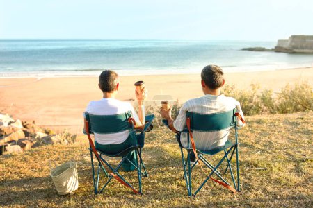 Photo for Weekend At Ocean. Senior Travelers Couple Sitting In Chairs Back To Camera And Drinking Coffee From Paper Cups, Looking At Beach And Sea Water Outside. Rear View Of Spouses Relaxing On Vacation - Royalty Free Image