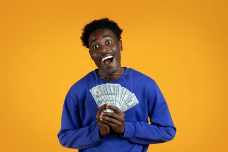 Cashback, loan, lottery, giveaway. Emotional happy rich wealthy handsome young african american guy in casual outfit holding money cash dollar banknotes and laughing, yellow studio background