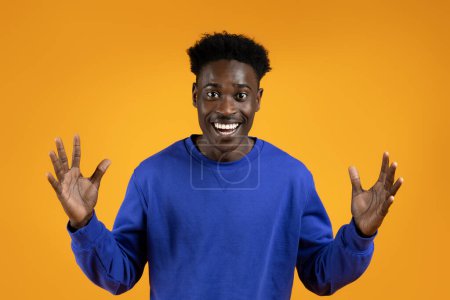 Photo for Studio portrait of amazed handsome young black guy in blue sweater gesturing and grimacing on yellow studio background, expressing amazement. Human emotions, gestures concept - Royalty Free Image