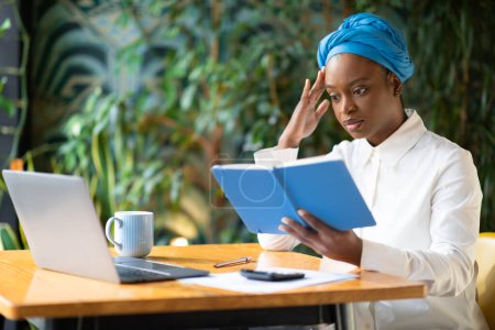 Photo for Business Troubles. Overwhelmed young black woman entrepreneur, small business owner facing financial challenges or losses, using laptop and calculator at cafe, checking her notes in notepad - Royalty Free Image
