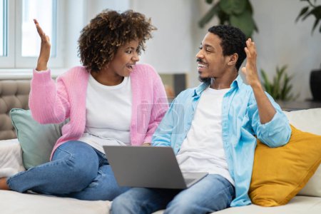 Photo for Lucky cheerful happy young beautiful black couple sitting on couch, gambling on Internet, raising hands up and exclaiming, using laptop at home. Cashback, online trading concept - Royalty Free Image