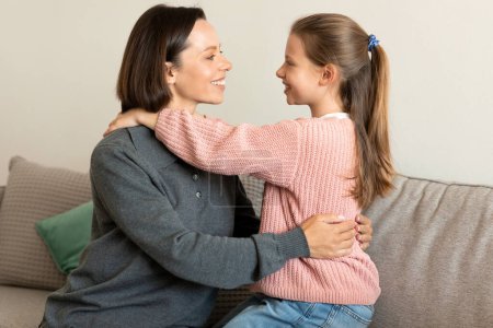 Photo for Cheerful pretty caucasian middle aged woman hugging small girl on sofa in living room interior. Love, relationship, family, communication at home in free time, daughter and mom - Royalty Free Image