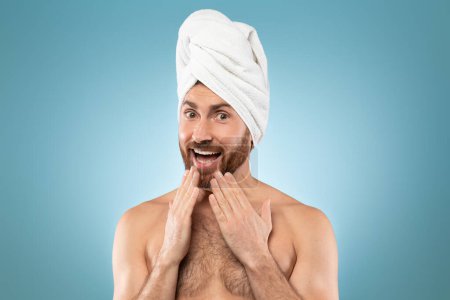 Téléchargez les photos : Humour bel homme d'âge moyen avec serviette blanche sur la tête regardant dans l'excitation à la caméra, posant sur fond bleu studio après la douche, espace de copie - en image libre de droit