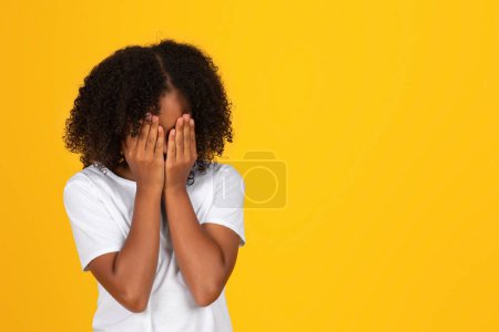 Foto de Infeliz adolescente triste rizado chica en camiseta blanca llorando, cierra la cara con las manos, sufren de estrés, aislado en el fondo del estudio amarillo. Problemas en la educación, acoso escolar, malas noticias y estrés - Imagen libre de derechos