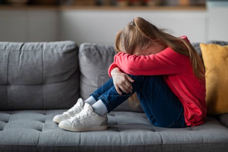 Photo for Kids Depression Concept. Upset Little Girl Crying At Home, Depressed Female Child Burying Head In Knees While Sitting On Couch In Living Room, Suffering Mental Breakdown, Copy Space - Royalty Free Image