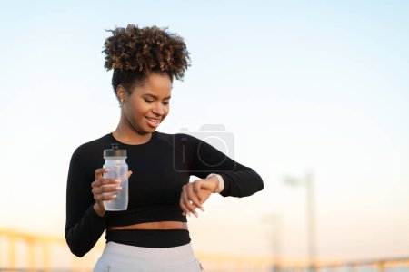 Photo for Smiling Black Female Jogger Checking Running Time On Smartwatch After Outdoor Training, Happy Young African American Woman Drinking Water And Checking Fitness Tracker Data On Watch, Copy Space - Royalty Free Image