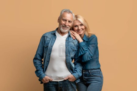 Photo for Beautiful happy elderly husband and wife wearing casual denim outfits posing together on colorful pastel background, senior couple cuddling and smiling at camera, studio shot - Royalty Free Image