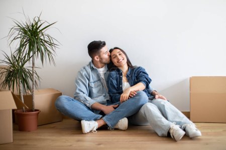 Portrait Of Smiling Romantic Young Couple Relaxing Among Cardboard Boxes After Moving To New Home, Cheerful European Spouses Embracing And Smiling, Enjoying Relocation Day, Copy Space
