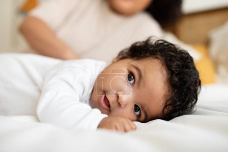 Foto de Sonriente dulce lindo bebé negro se encuentra en la cama blanca con mamá, descanso, relajarse en el dormitorio. Recién nacido, infancia, vacaciones de cuidado infantil, paternidad en casa, anuncio y oferta, primer plano - Imagen libre de derechos