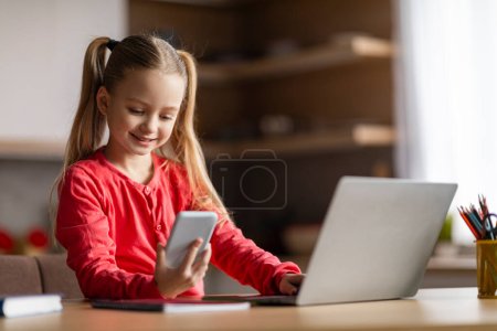 Photo for Kids And Gadgets. Smiling Little Girl Using Smartphone And Laptop At Home, Cute Preteen Female Kid Browsing Internet On Mobile Phone Or Checking New Game App, Enjoying Digital Leisure - Royalty Free Image
