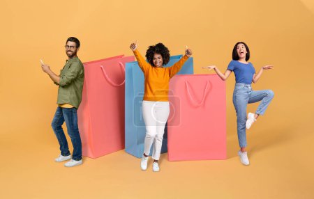 Photo for Positive multicultural young friends two pretty ladies and one guy using cell phone posing with huge shopping bags over colorful background, millennial enjoying black friday sale, collage - Royalty Free Image