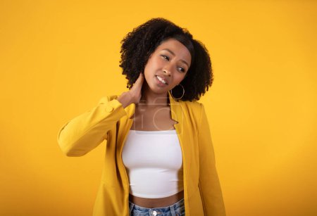 Photo for Despaired sad black curly woman suffering from neck pain, making massage, standing on yellow background. Health problems, muscle pain after training, overwork and arthritis, injury - Royalty Free Image