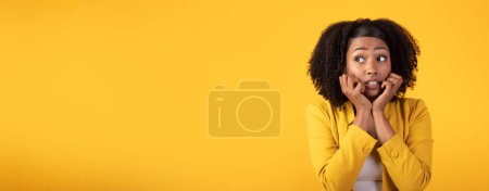Téléchargez les photos : Effrayé anxieux terrifiant dame noire dans occasionnel avec des cheveux touffus geste et regarder de côté l'espace libre à quelque chose d'effrayant sur fond de studio jaune, panorama - en image libre de droit