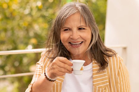 Téléchargez les photos : Heureux souriant femme caucasienne âgée aux cheveux gris boire une tasse de café dans le café, en plein air, gros plan. Dame jouit de repos et de détente seul, temps libre le matin, week-end en été - en image libre de droit
