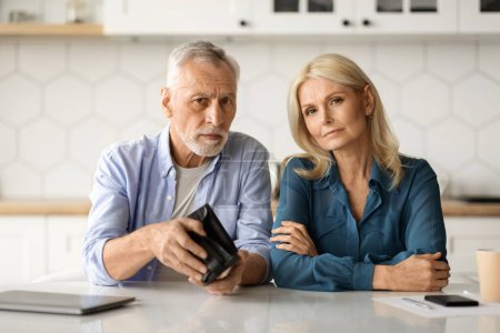 Photo for Financial Problems. Upset Senior Couple Showing Empty Wallet While Sitting At Table In Kitchen, Mature Husband And Wife Suffering Retirement Crisis, Having Economy Isuues, Looking At Camera - Royalty Free Image