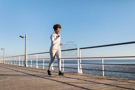 Photo for Outdoor Sports. Motivated Young African American Woman Running On Pier Near Sea, Smiling Millennial Black Lady In Sportswear Jogging Outside, Enjoying Cardio Training, Full Length, Copy Space - Royalty Free Image