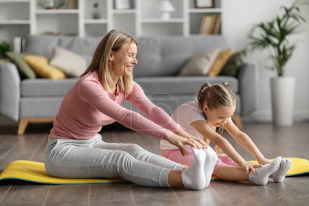 Téléchargez les photos : Joyeux jeune mère et petite fille étirant les jambes ensemble à la maison, famille sportive faisant des exercices matinaux sur des tapis de yoga dans le salon confortable, profiter des séances d'entraînement domestiques, copier l'espace - en image libre de droit