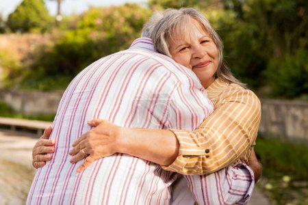 Photo for Positive smiling senior caucasian wife and husband hugging in park at weekend, spare time, outdoor. Couple enjoy active lifestyle, date, love and relationship, rest together - Royalty Free Image