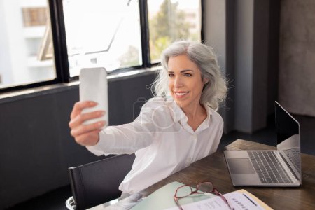 Photo for Business Blogging. Cheerful Manager Lady Making Selfie On Phone, Sharing Her Professional Success Online In Social Media App, Posing Sitting In Modern Office Interior. Workplace Fun Concept - Royalty Free Image