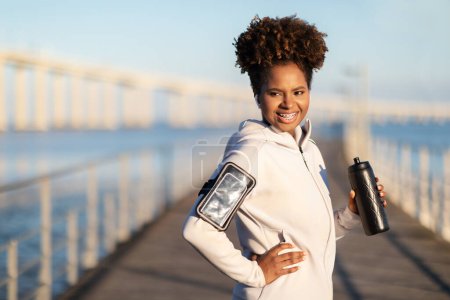 Photo for Beautiful Black Female Jogger With Armband And Water Bottle Posing Outdoors, Happy Young African American Woman In Sportswear Relaxing After Fitness Training, Enjoying Outside Workouts, Copy Space - Royalty Free Image