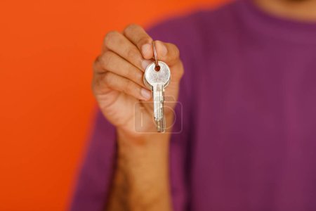 Photo for Cropped of dark-skinnes guy holding the keys with keychain from new house, isolated on orange background. Keys from new property in male hand, happy buyer of own estate. Guy relocated - Royalty Free Image