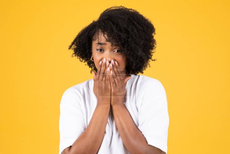 Photo for Sad shocked millennial african american curly woman in white t-shirt presses hands to face, crying, isolated on yellow studio background. Tears of joy, good or bad news, ad and offer, emotions - Royalty Free Image