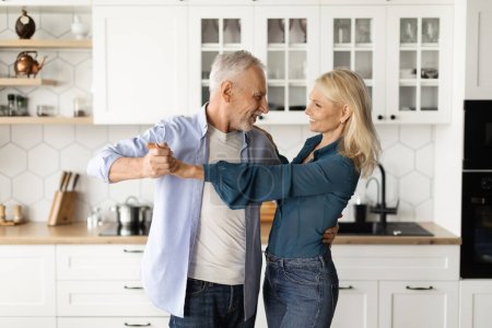 Téléchargez les photos : Portrait de couple de personnes âgées romantiques dansant ensemble à l'intérieur de la cuisine, Conjoints matures heureux tenant la main et se regardant, Profitant de passer du temps ensemble à la maison, Copier l'espace - en image libre de droit