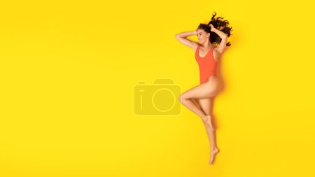 Téléchargez les photos : Offre vacances d'été. Happy Fit femme en maillot de bain orange posant regardant à côté de l'espace de copie, la publicité Grande offre de mode et de beauté sur fond jaune studio. Panorama, Vue sur le dessus - en image libre de droit