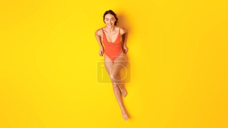 Foto de Disfruta Summer. Mujer joven feliz en traje de baño naranja relajante con los ojos cerrados tomando el sol tumbado en el estudio sobre fondo amarillo, Panorama. Vacaciones junto al mar Concepto de ocio y relajación - Imagen libre de derechos