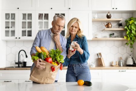 Photo for Food Expenses. Stressed Senior Couple In Kitchen Checking Bills After Grocery Shopping, Frustrated Elderly Husband And Wife Counting Household Spends, Confused By Big Prices, Copy Space - Royalty Free Image