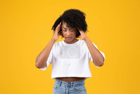 Photo for Despaired tired millennial african american curly woman in white t-shirt presses hands to temples, suffering from headache, isolated on yellow studio background. Health problems, fatigue, migraine - Royalty Free Image
