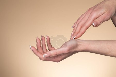 Photo for Beautiful middle aged woman hands. Female applying cream or lotion over beige studio background, copy space. Spa and manicure, soft skin, skincare concept - Royalty Free Image